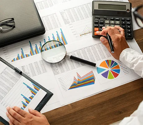 Uomo che analizza grafici e dati finanziari con una calcolatrice, lente d'ingrandimento e documenti.