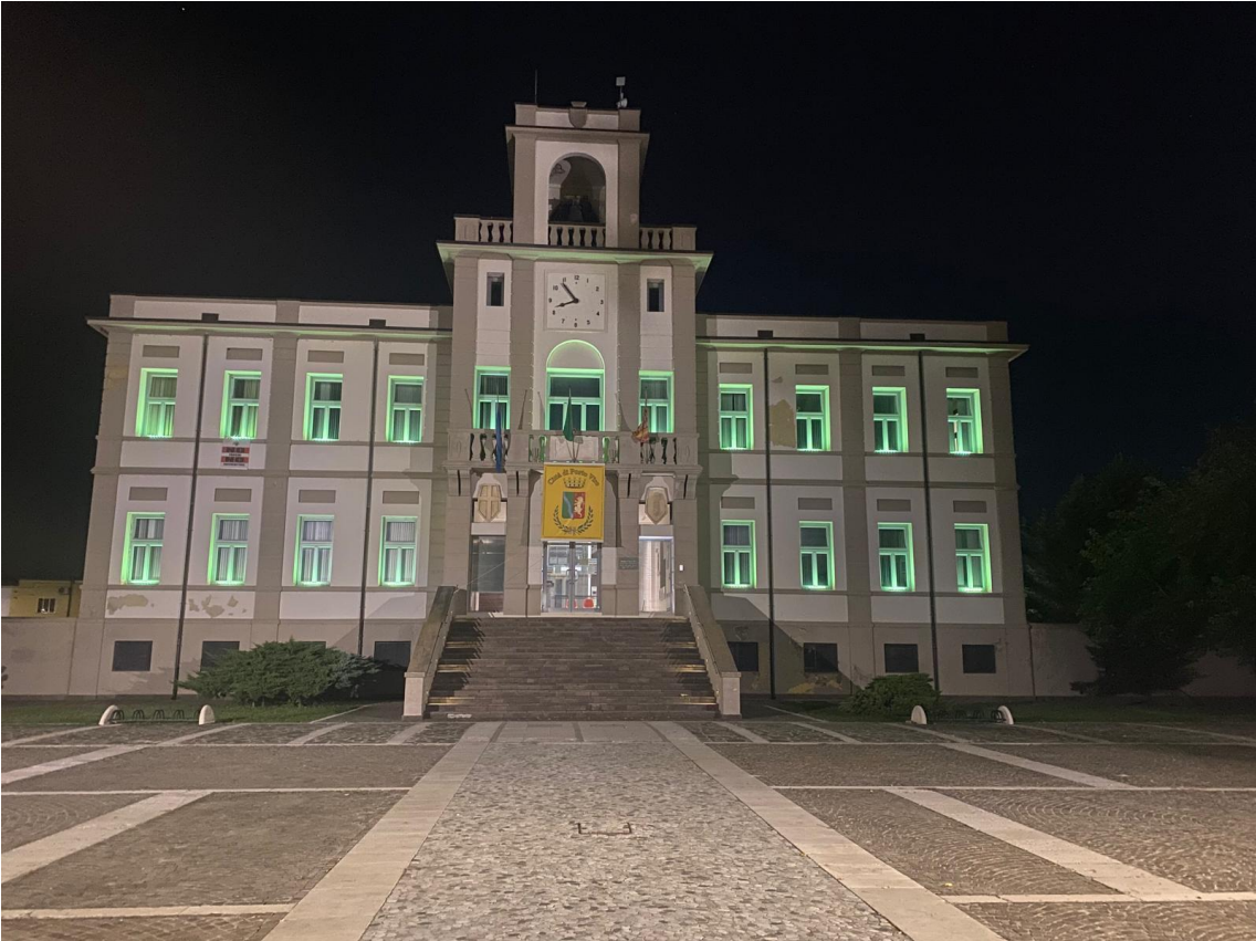 Edificio comunale di Porto Viro illuminato di notte con luce verde, facciata classica e orologio centrale.